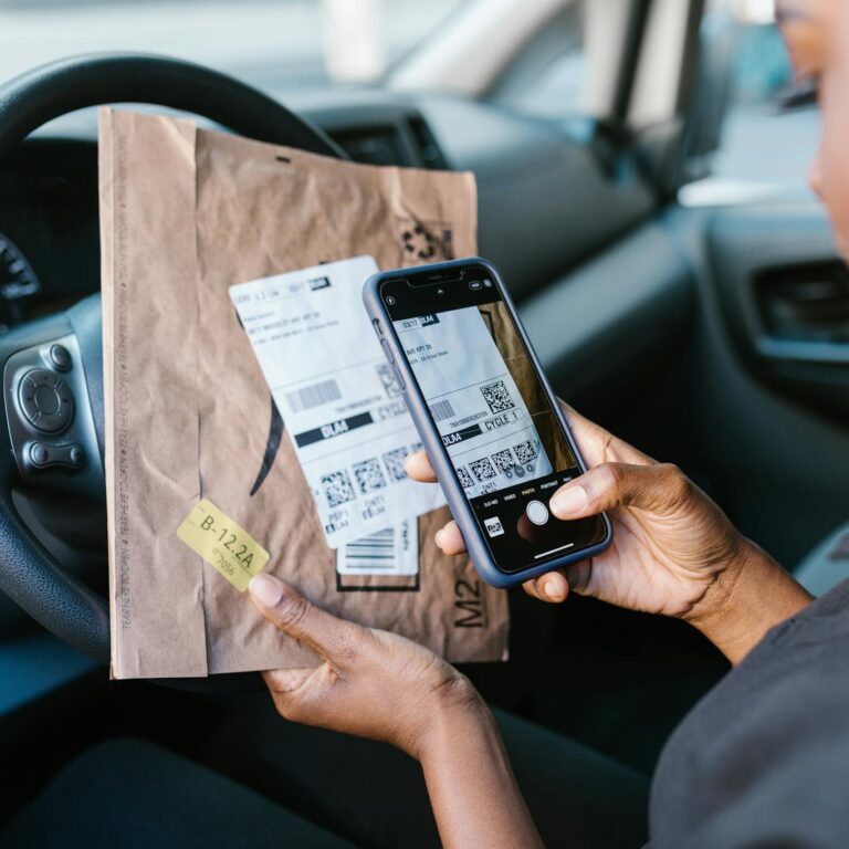 Close-up of a courier in a car scanning a package label with a smartphone for delivery service.